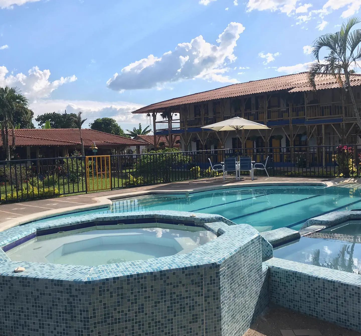 Jacuzzi de mosaico junto a la piscina, con la casona de guadua de dos pisos al fondo bajo un cielo azul